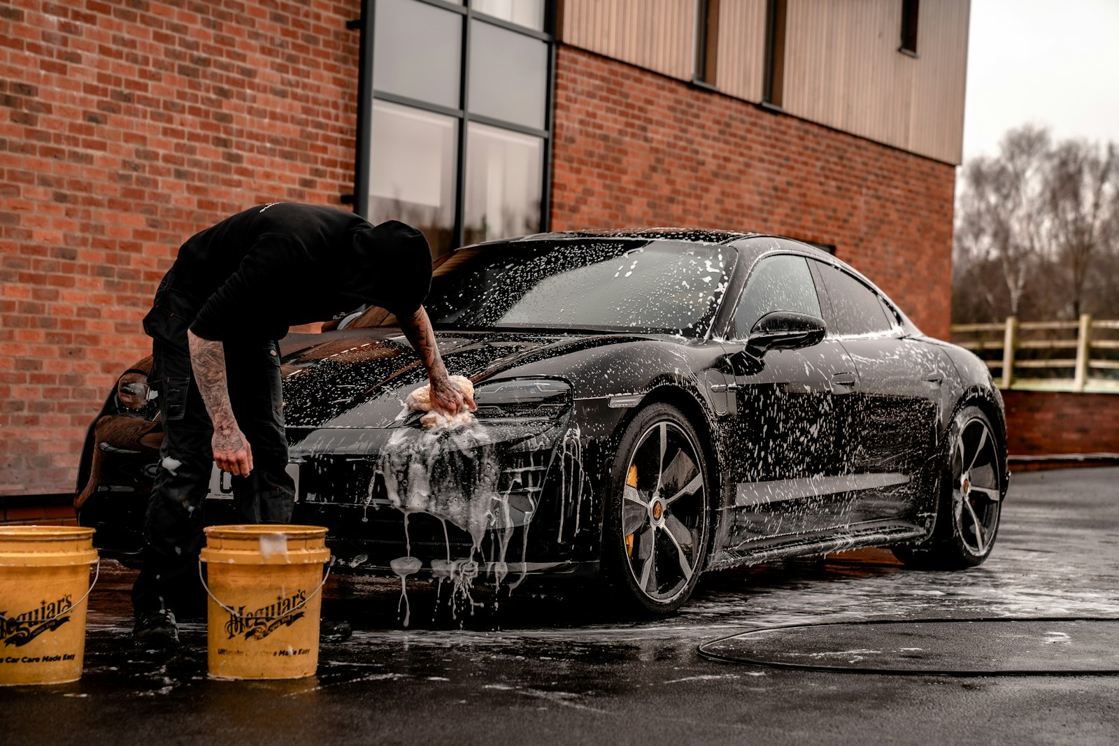 A dark sedan covered in soap suds being washed by hand